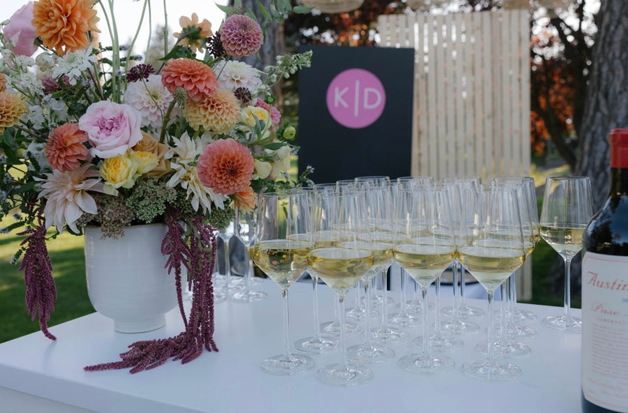 Table with floral arrangement, wine glasses, and a bottle of wine. The beautiful flowers are designed by wedding florist Daisies in May flower farms