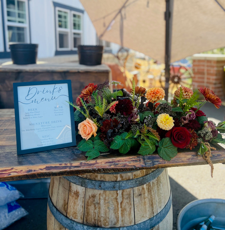 Fall Floral arrangement on a wooden barrel with a drink menu in an outdoor setting