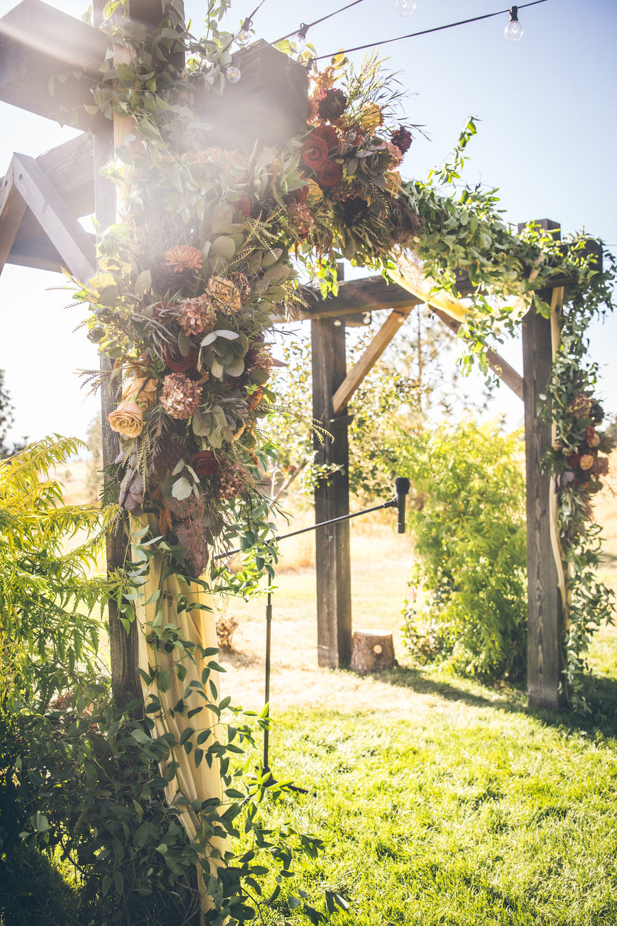 Decorative wooden arch with floral arrangements by Daisies in May for a rustic outdoor wedding.