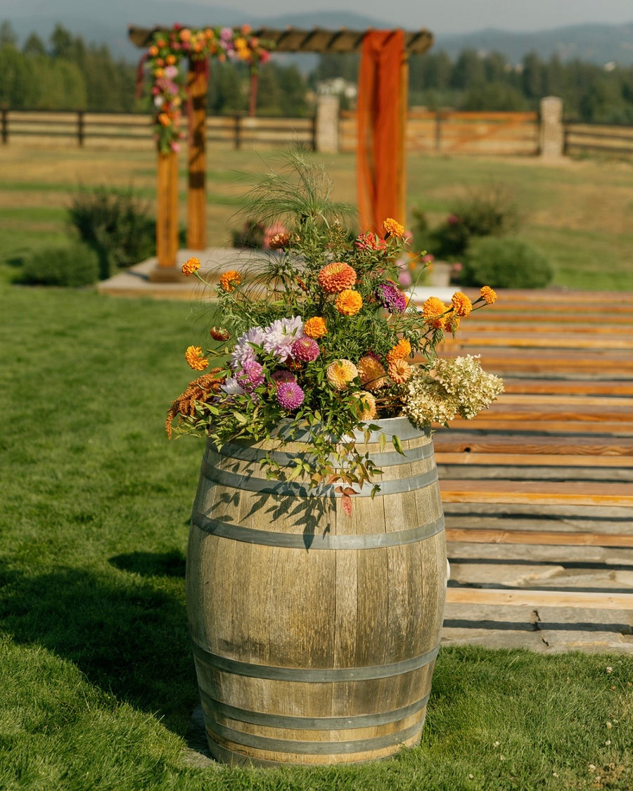 Spokane, WA florist created a decorative floral arrangement on a wooden barrel with a rustic wedding arch in the background.