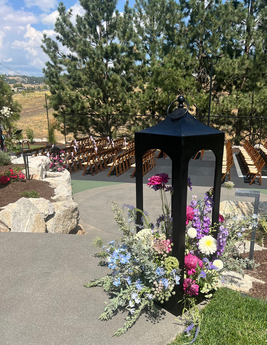 Decorative floral arrangement with a black lantern in front of an outdoor wedding set in Spokane, WA.
