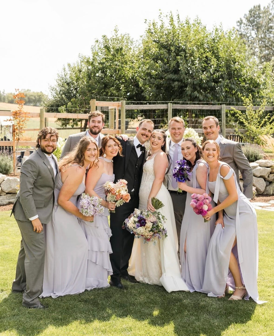 Wedding party posing outdoors with greenery in the background. Bridal and bridesmaid's bouquets were crafted by Daisies in May wedding florist.