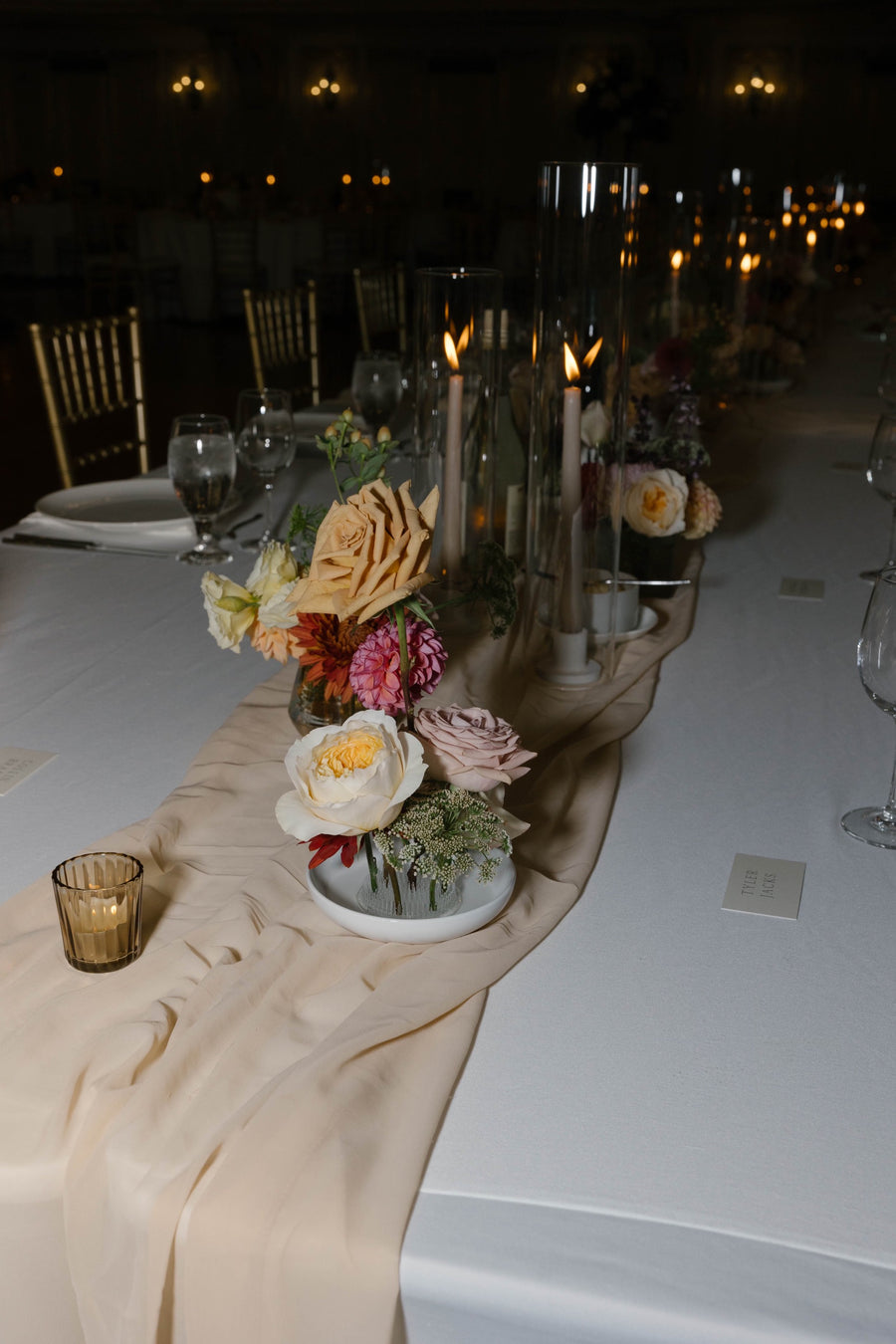 Decorative table setting with flowers and candles on a white tablecloth at night.