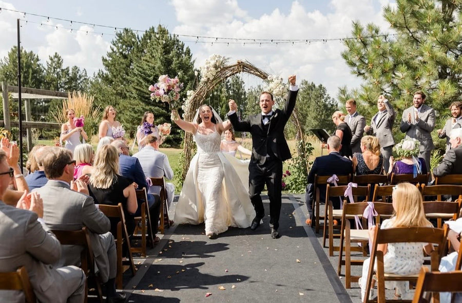 Wedding ceremony with bride and groom walking down the aisle, surrounded by guests. Bride is holding up her gorgeous bouquet by florist Daisies in May.