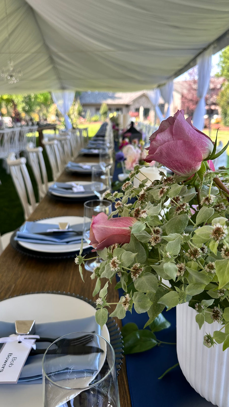 Decorative table setting with pink flowers and plates under a tented outdoor canopy.