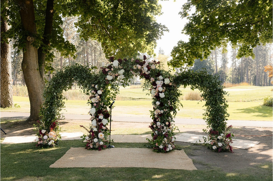 Trinity arch adorned with greenery, crimson, white, and pink flowers for a beautiful wedding at Manito Country Club in Spokane, WA